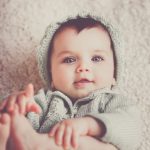 baby on gray knit clothes and cap lying on carpet