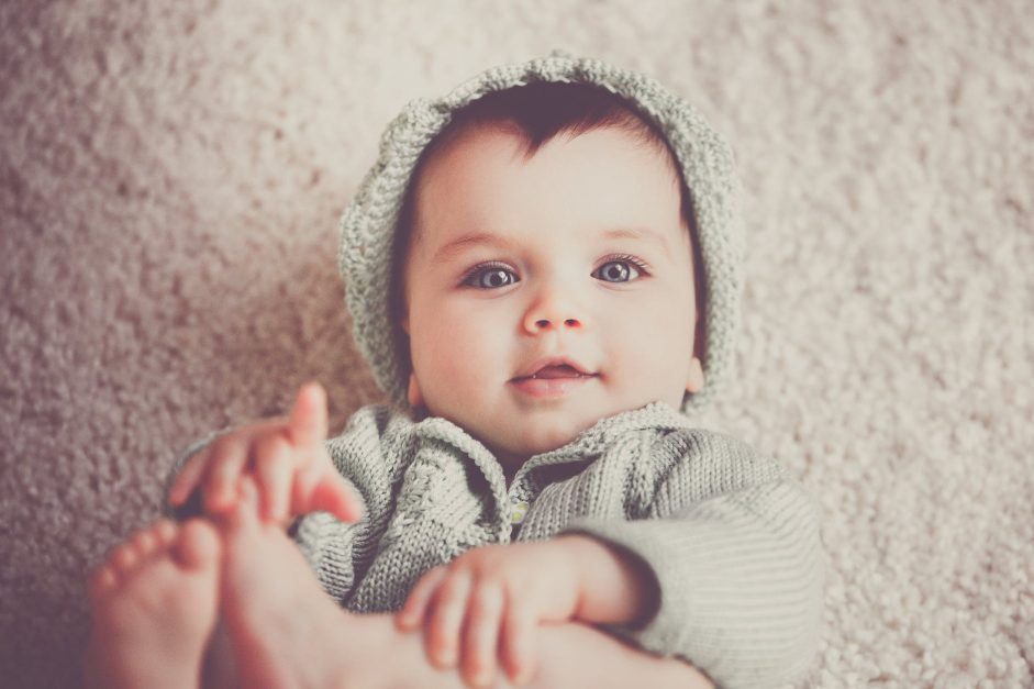 baby on gray knit clothes and cap lying on carpet