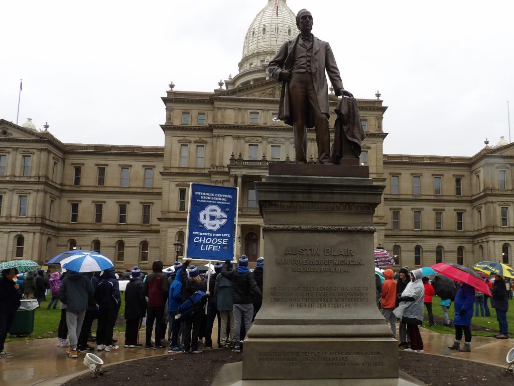 People gather in the rain to rally and march around MI's capitol, November 8, 2023.